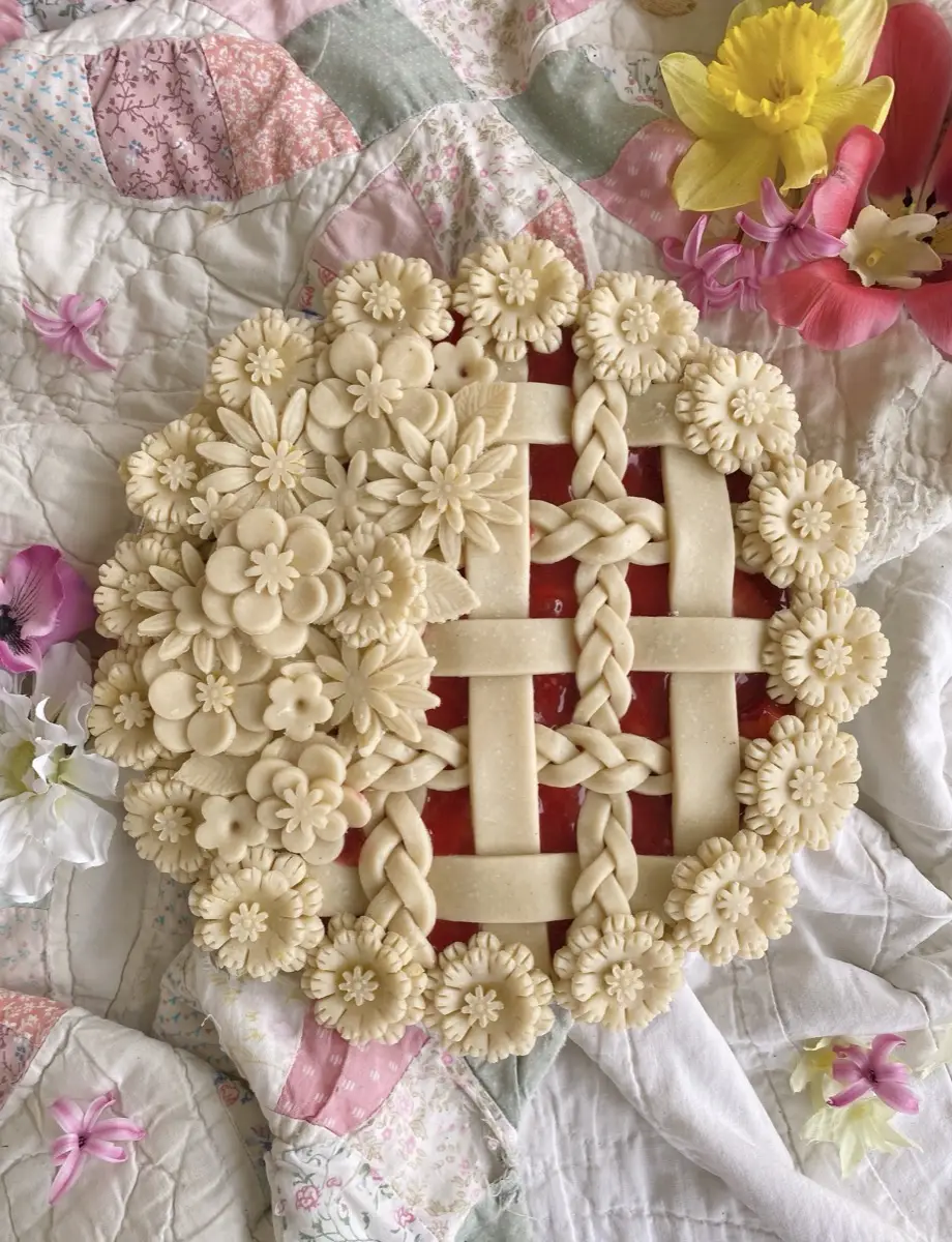 Birdie’s lattice pie with hand-cut pastry flowers, nestled on a pink patchwork quilt beside spring blooms